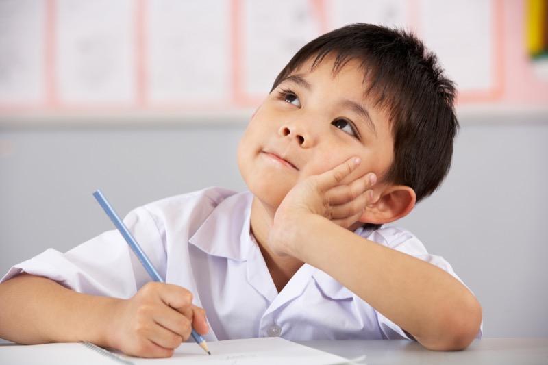 Comprender textos La imagen muestra a un niño con un texto y un lápiz en su mano mirando hacia arriba con gestos de pensamiento