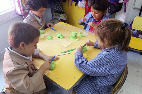 Propiedades de objetos La imagen muestra a niños y niñas en una mesa de trabajo realizando figuras con arena para moldear