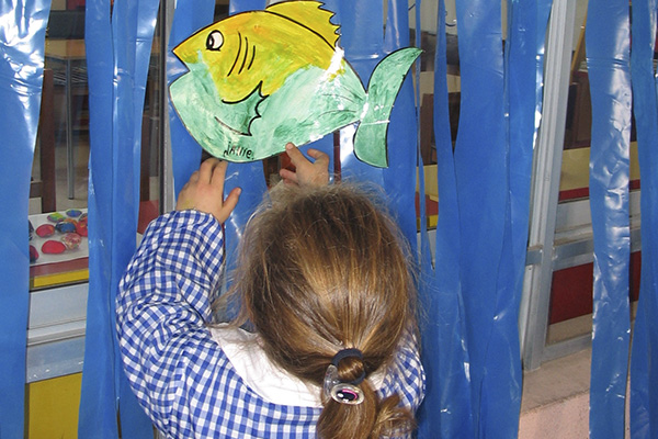 Animales La imagen muestra a una niña pegando un dibujo de un pez en un fondo de plástico azul