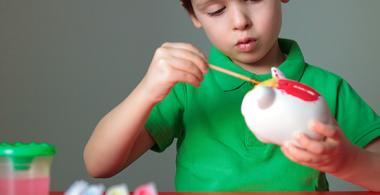 La imagen muestra a un niño pintando una alcancía con forma de cerdito de yeso