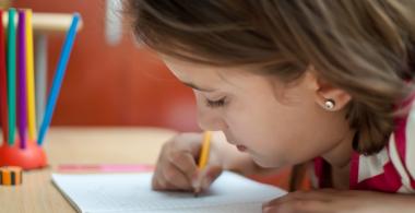 La imagen muestra una niña escribiendo en un cuaderno