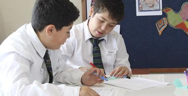 La imagen muestra a dos estudiantes leyendo un texto en conjunto