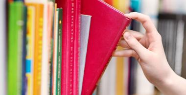 La imagen muestra un estante de libros y una mano escogiendo uno de los textos