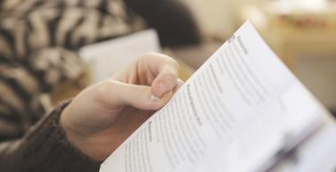 La imagen muestra un libro abierto y una mano que lo sostiene en posición de lectura