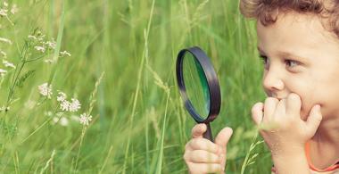 La imagen muestra a un niño con una lupa observando flores