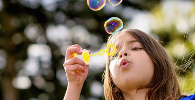 En la imagen se observa a una niña creando burbujas de jabón